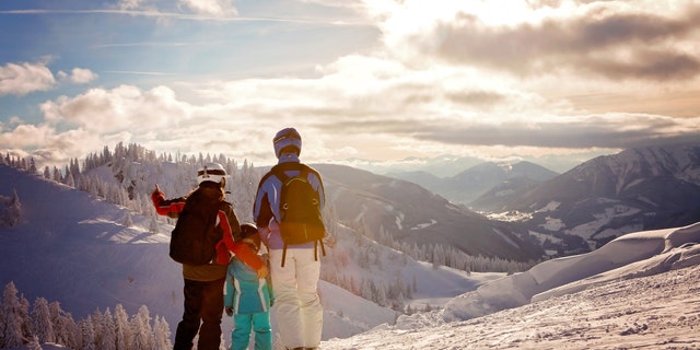 Happy family in winter clothing at the ski resort, winter time, watching at mountains in front of them