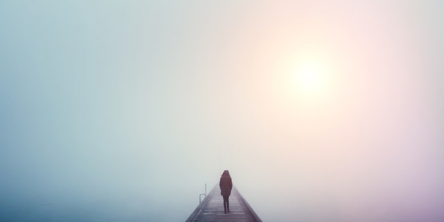 Woman crossing the bridge over lake on a foggy winter day.