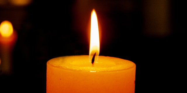 single burning candle on a dark background with reflection