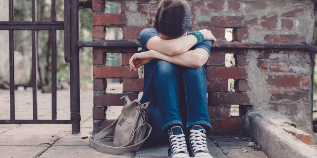 Crying girl with head in hands sitting on the ground