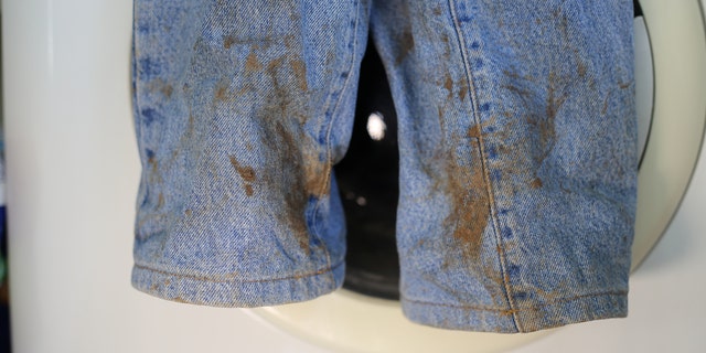 Muddy jeans on a washing machine. Mud stain on jeans. Stained jeans before laundry.