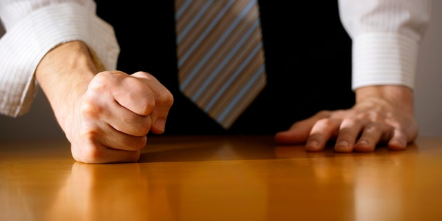 A DSLR photo of a businessman hitting the table with clenched fist. Can illustrate the concept of stress, disagreemnet, anger, etc.