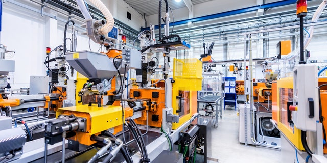 Horizontal color image of large group of automated injection moulding machines for plastic parts production.