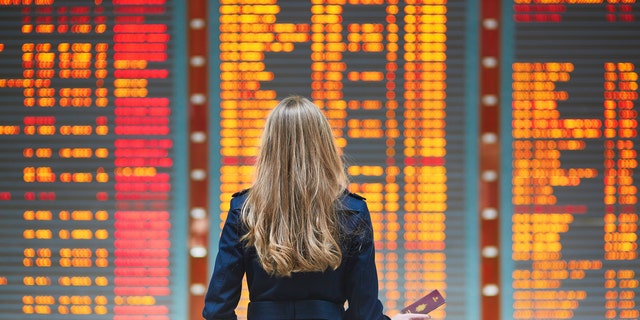 Young woman in international airport looking at the flight information board, checking her flight
