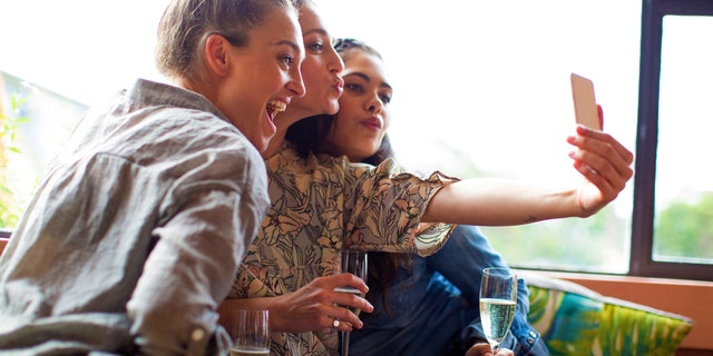Mixed race girlfriends with Aboriginal woman taking selfie at bar