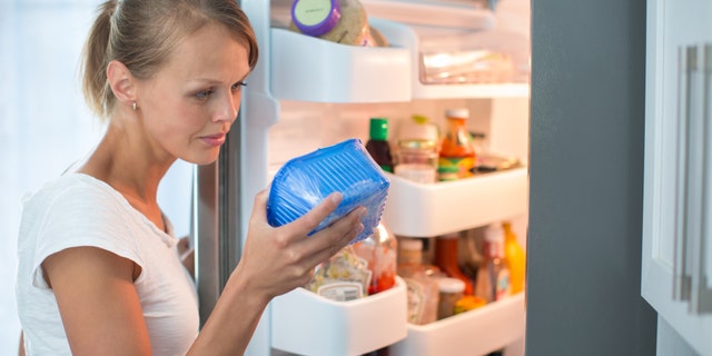Is this still fine? Pretty, young woman in her kitchen by the fridge, looking at the expiry date of a product she took from her fridge -