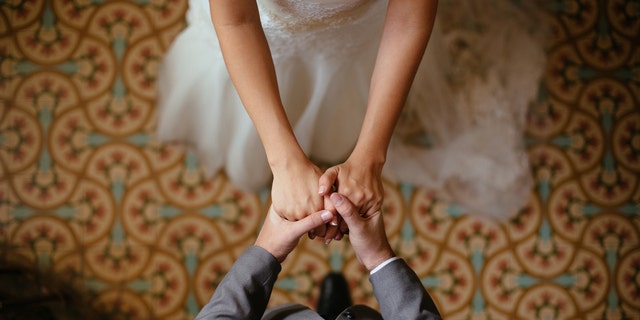 A close up shot of a bride and groom holding hands from a top view.
