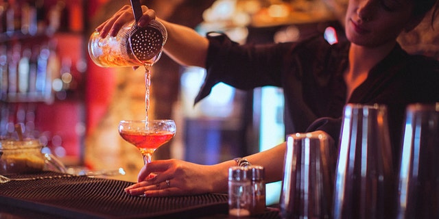 Close-up of a young female bartender pouring cocktail in a nightlife cocktail bar. Selective focus. Focus on foreground.