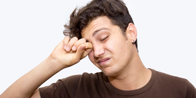 Portrait of napping young man rubbing his eyes isolated on white. Horizontal composition. Studio shot. Image developed from RAW format. Tired teenage boy has got short, curly, brown hair.