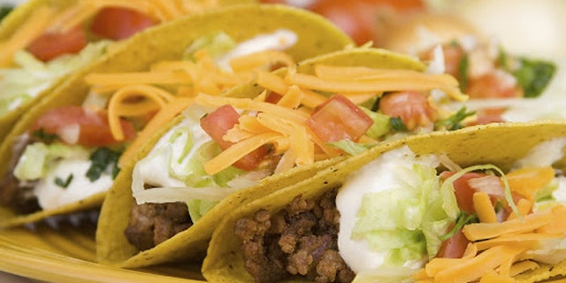 A plate of freshly prepared ground beef tacos, with tomato, freshly grated cheese, lettuce and sour cream.