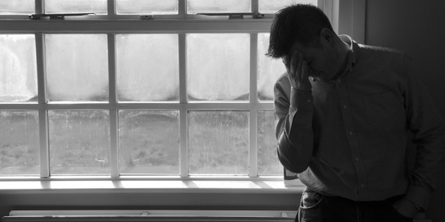 Lone anonymous middle aged man suffering depression or anxiety. Â Looking sad, worried, frustrated, in pain or desperate with hands on head leaning against an empty white wall.