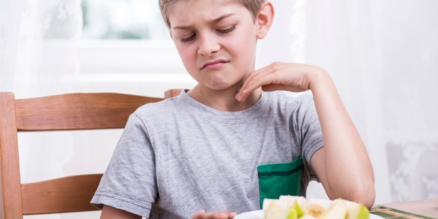 Blonde boy refusing to eat healthy apple