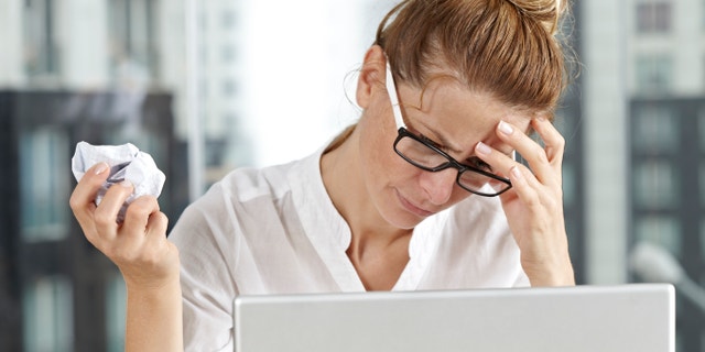 A frustrated businesswoman having headache and crumpling paper