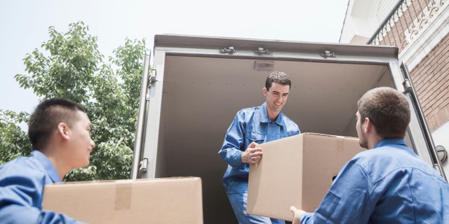 Movers unloading a moving van, passing a cardboard box