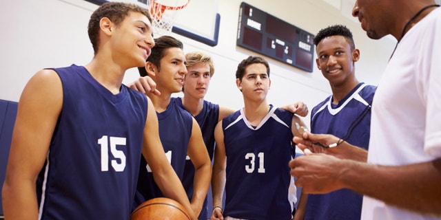 Male High School Basketball Team Having Team Talk With Coach In Gymnasium