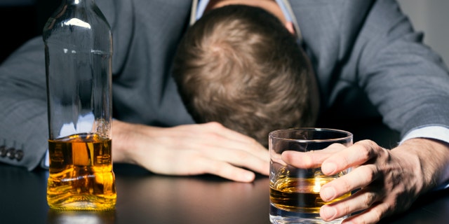 alcohol addiction - drunk businessman holding a glass of whiskey on the table