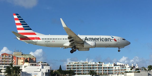 An American Airlines plane zooms over beachgoers.