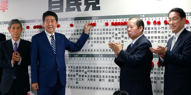 Japanese PM Shinzo Abe poses for photos as he marks on the name of one of those elected in the parliamentary lower house election in Tokyo, Sunday, Oct. 22, 2017.