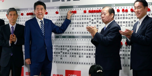 Japanese PM Shinzo Abe poses for photos as he marks on the name of one of those elected in the parliamentary lower house election in Tokyo, Sunday, Oct. 22, 2017.