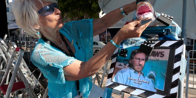 Cinema fan Martine Santoro adjusts a model of a shark as featured in the movie 'Jaws' by director and president of the 66th Cannes Film Festival, Steven Spielberg, on her step ladder in front of the Festival Palace during the Festival in Cannes May 19, 2013. REUTERS/Eric Gaillard (FRANCE - Tags: ENTERTAINMENT) - RTXZSEY