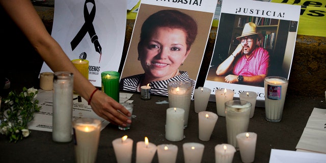 In this May 16, 2017, file photo, a woman places a candle in front of pictures of murdered journalists Miroslava Breach, left, and Javier Valdez during a demonstration against the killing of journalists, outside the Interior Ministry in Mexico City.
