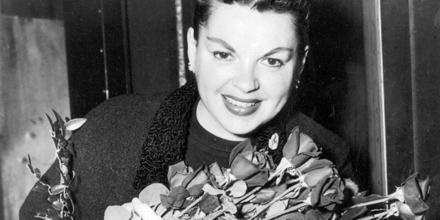 Judy Garland poses with long-stemmed roses in her arms as she arrives in New York City on Sept. 17, 1956. The singer-actress is to begin rehearsals for her Sept. 26 Palace Theater engagement. (AP Photo)