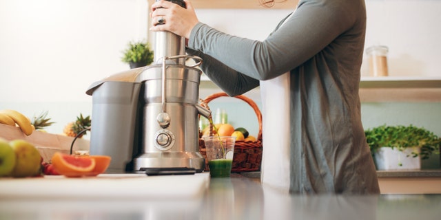 Cropped shot of young female bar employee making fruit juice using juicer machine at counter.