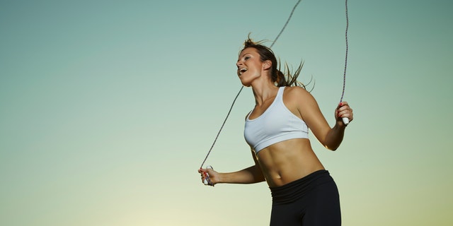 Young fitness woman used a skipping rope, sun and sky on background, copy space