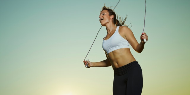 Young fitness woman used a skipping rope, sun and sky on background, copy space