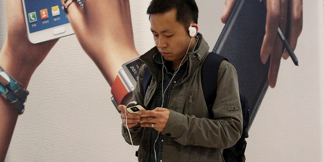 April 8, 2014: A man uses a smartphone near an advertisement for Samsung Electronics Co.'s Galaxy Note 3 in Seoul, South Korea.