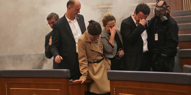 Feb. 26, 2016: Opposition lawmakers cover their eyes as smoke fills the auditorium of the Kosovo assembly after they released tear gas canisters disrupting a parliamentary session in Kosovo capital Pristina.