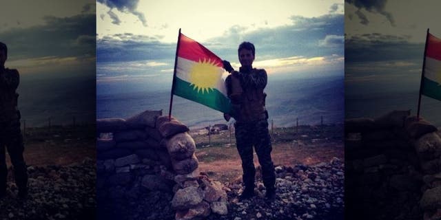 Kurdish Peshmerga soldier waves the Kurdish flag while manning a front line in the battle against ISIS