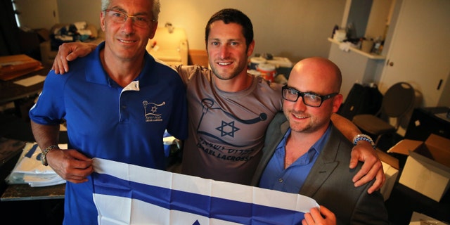 July 15, 2014: In this Israel Lacrosse head coach Bill Beroza, left, attackman Noach Milller, center, and team executive director Scott Neiss hold an Israeli flag inside a hotel room used to organize team gear, in Commerce City, Colo.