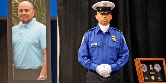 A TSA officer stands in front of a portrait of slain TSA officer Gerardo Hernandez during his public memorial at the Los Angeles Sports Arena.