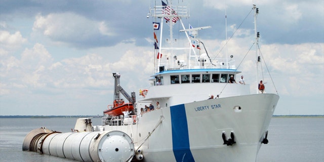 NASA's solid rocket booster recovery ship Liberty Star closes in on the shore with a spent rocket alongside.