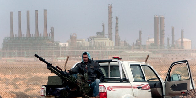 FILE - In this March 5, 2011 file photo, an anti-government rebel sits with an anti-aircraft weapon in front an oil refinery in Ras Lanouf, eastern Libya. The fight for Libyas Ras Lanuf refinery and nearby Sidr depot threatens to spiral into open conflict between rival factions vying for power from east and west. With both sides claiming the facilities as their own but control unclear, decisive days lie ahead. (AP Photo/Hussein Malla, File)