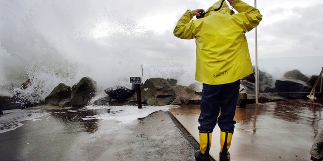 CARDIFF BY THE SEA, CA - DECEMBER 20:  Encinitas fireman Mike Kemp adjusts his hood as a wave crashes over a sea wall December 20, 2002 in Cardiff By the Sea, California. Heavy rains and large surf pounded the West Coast as a product of El Nino with the region expecting above average rainfall totals this winter due to El Nino.  (Photo by Sandy Huffaker/Getty Images)