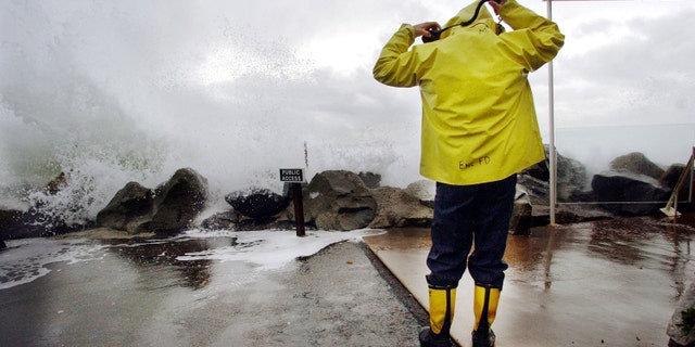 CARDIFF BY THE SEA, CA - DECEMBER 20: Encinitas fireman Mike Kemp adjusts his hood as a wave crashes over a sea wall December 20, 2002 in Cardiff By the Sea, California. Heavy rains and large surf pounded the West Coast as a product of El Nino with the region expecting above average rainfall totals this winter due to El Nino. (Photo by Sandy Huffaker/Getty Images)