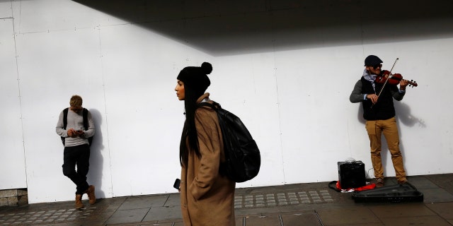 A man looks at his mobile phone next to a busker in Oxford Street, London.