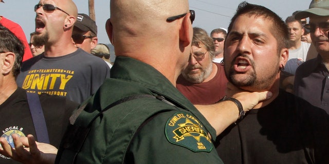 A Cowlitz County Sheriff grabs a union worker by the throat as police move in on several hundred union workers blocking a grain train in Longview, Wash., Wednesday, Sept. 7, 2011.