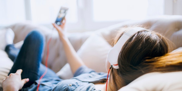 Cheerful young woman listening music in headphones on her mobile phone