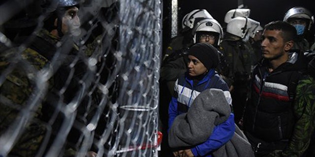 Refugees wait to cross the Greek-Macedonian border as policemen from both sides stand guard, near the northern Greek village of Idomeni, Thursday, Dec. 3, 2015. Greek riot police struggled to restore order Thursday after chaotic clashes between asylum-seekers at the country's border with Macedonia. (AP Photo/Giannis Papanikos)
