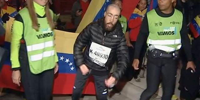 This photo from video provided by Ken Herzlich of Embargo Chicago shows Maickel Melamed, 38, center, of Venezuela, who has muscular dystrophy, nearing the finish line early Monday, Oct. 14, 2013, to be the last runner to finish the Chicago Marathon.