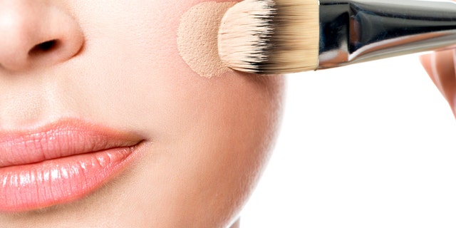 Makeup artist applying liquid tonal foundation on the face of the woman. Closeup photo of cheek