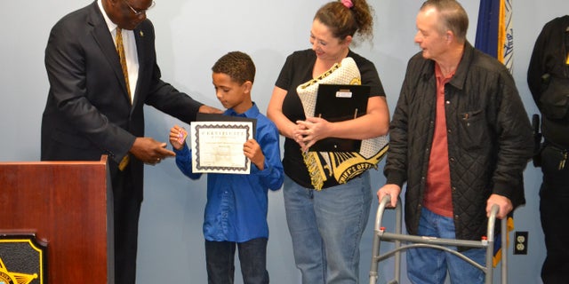 Malachi’s mother, April Coffey (center), and Allen Clemmons ( far right) stand as Sumter County Sheriff Anthony Dennis presents Malachi with a certificate naming him honorary employee of the month.