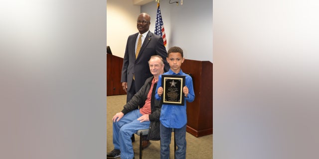 Malachi Coffey (right) stands next to Allen Clemmons (center) and Sumter County Sheriff Anthony Dennis (left). The sheriff's office presented Malachi with a plaque for his heroic deed.