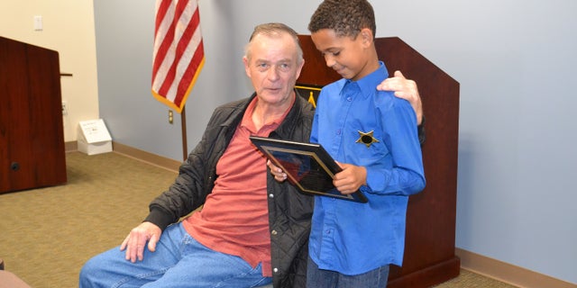 Malachi Coffey inspects his plaque as he stands next to Allen Clemmons. The 65-year-old man was nearly crushed by his Mustang convertible on March 10.