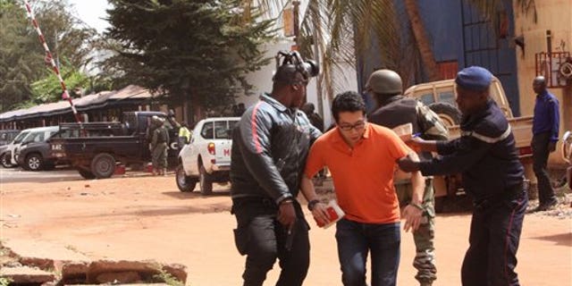 Mali trooper assist a hostage, centre, to leave the scene, from the Radisson Blu hotel to safety after gunmen attacked the hotel in Bamako, Mali, Friday, Nov. 20, 2015. Islamic extremists armed with guns and throwing grenades stormed the Radisson Blu hotel in Mali's capital Friday morning, killing at least three people and initially taking numerous hostages, authorities said. (AP Photo/Harouna Traore)