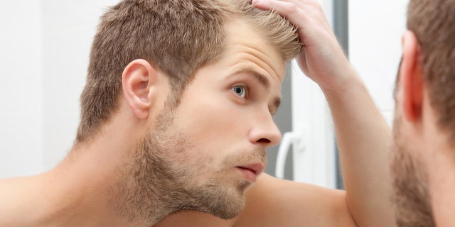 Handsome unshaven man looking into the mirror in bathroom