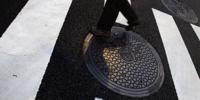 A pedestrian passes a manhole.
